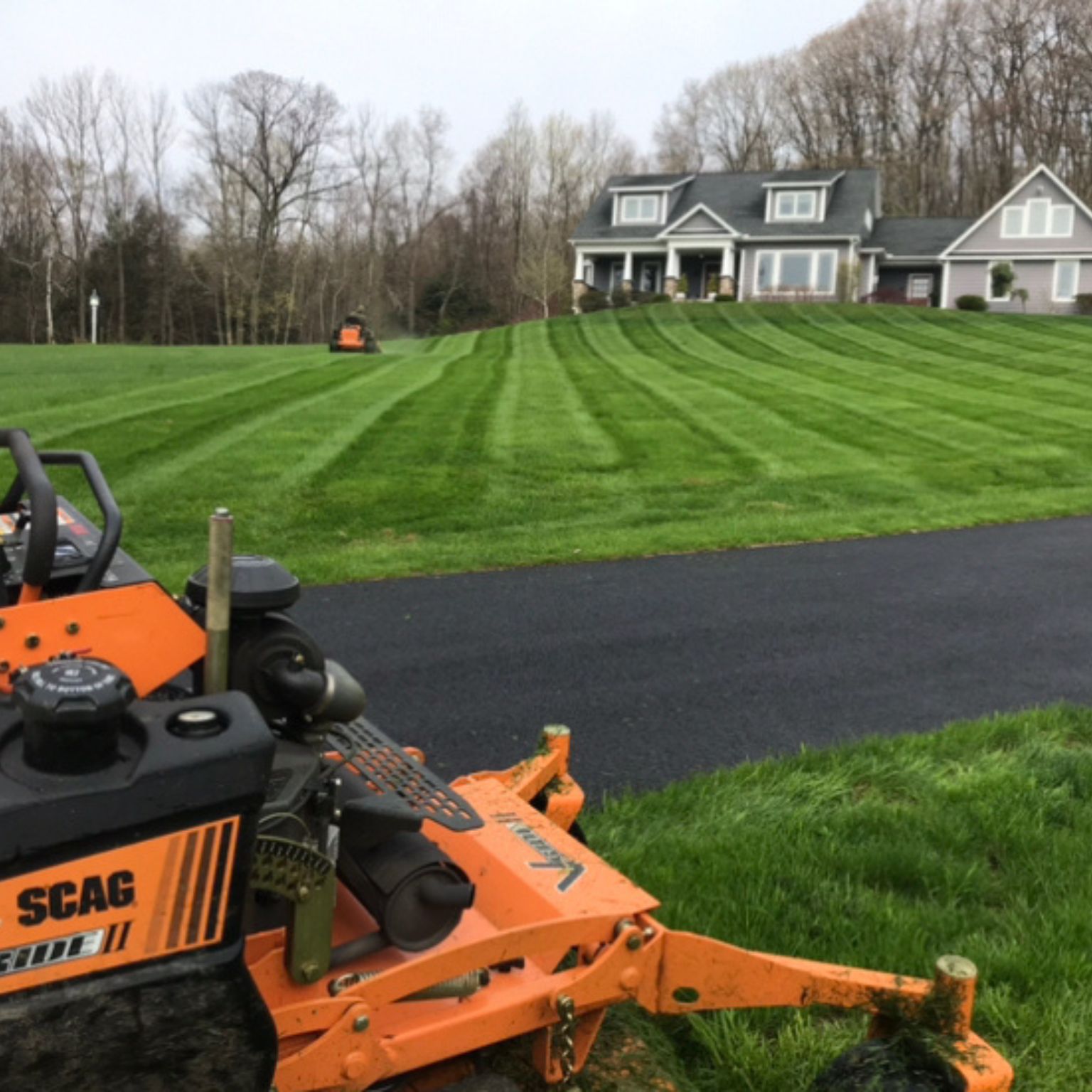 Good Lawn Care Watertown on a sloped front lawn with a black driveway and house in the background