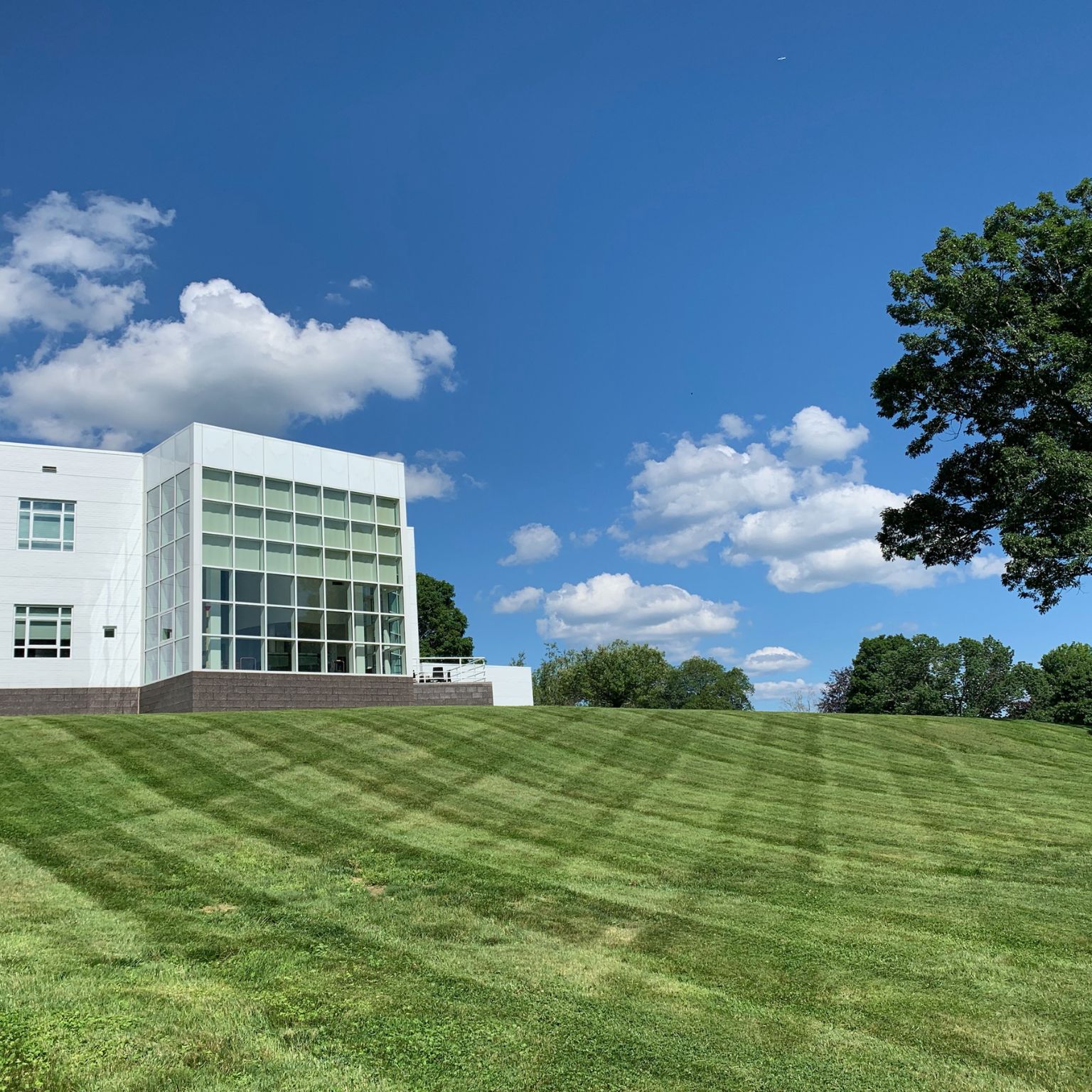 lawn maintenance Watertown CT on a sloped lawn beside a modern building under a bright blue sky