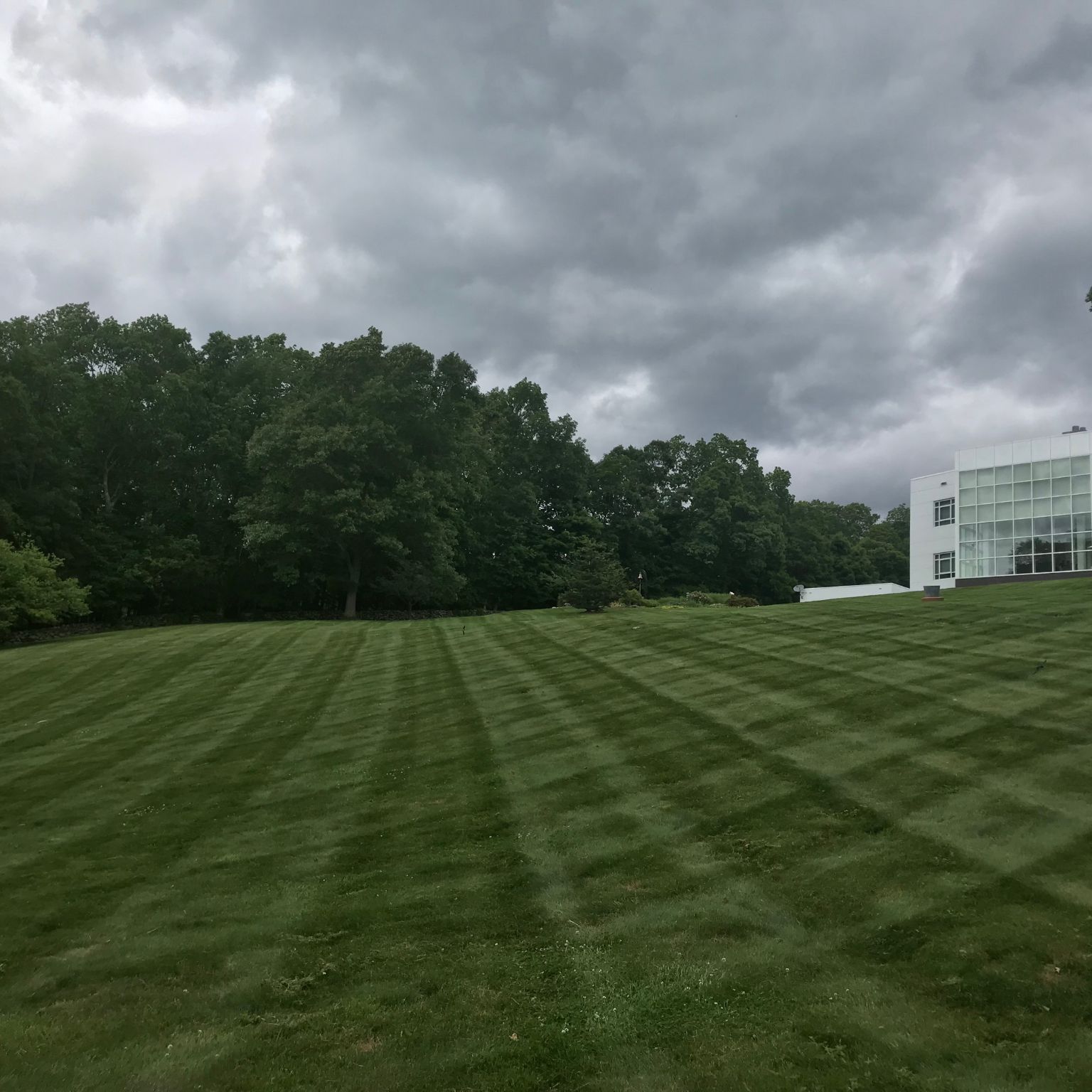 lawn mowing service Watertown CT on a striped lawn under dark storm clouds near a modern white building
